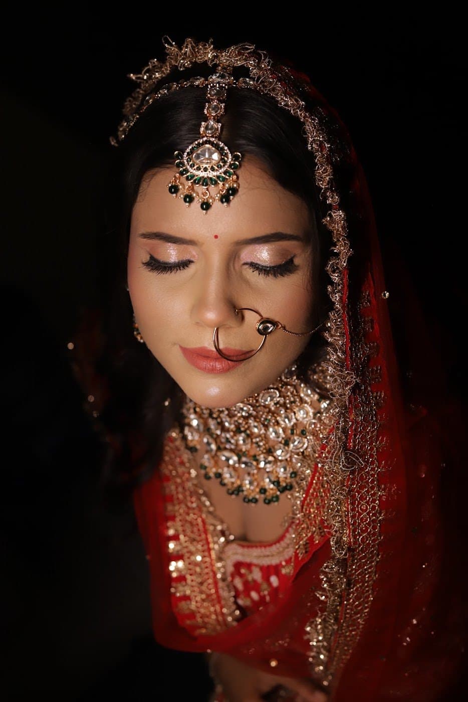 Bride with matha patti and nath in moody low-light portrait