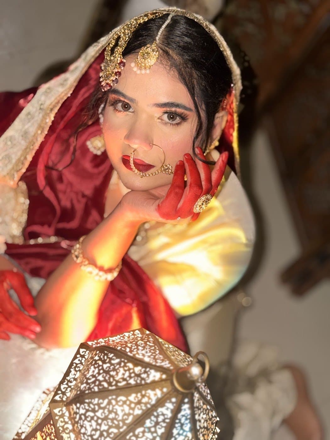 Bride posing with a golden lantern, bold red lips and mehendi