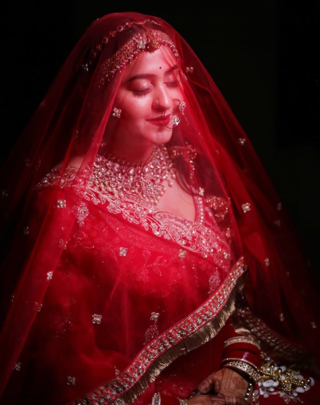 Bride under a red embroidered veil with soft glowing bridal makeup