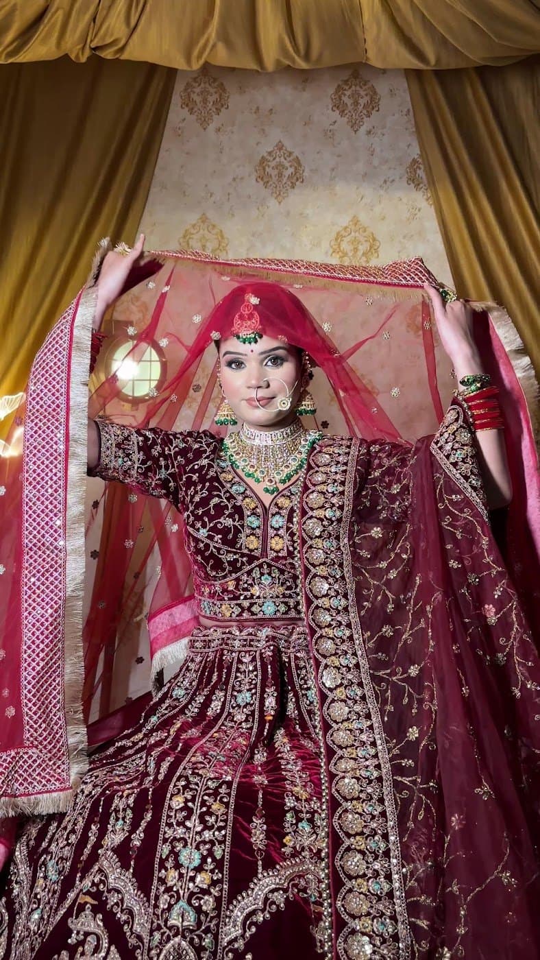Bride lifting her veil in a maroon velvet lehenga